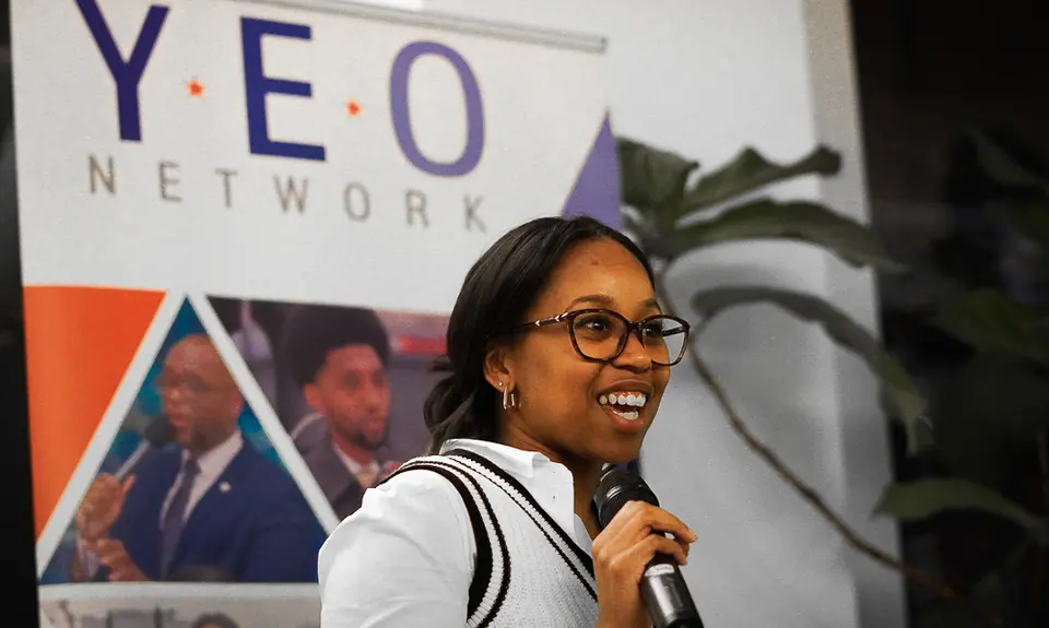 Woman speaking into a microphone in front of a sign that says YEO Network
