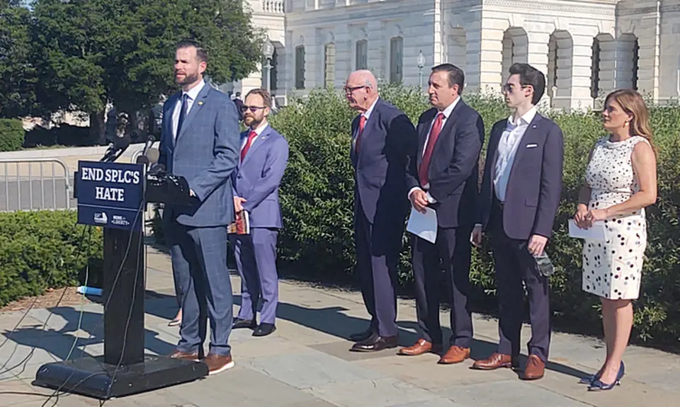 Photo shows Rep. Clay Fuller (R-GA) standing outside the US Capitol at a lectern with a sign that says "End SPLC Hate." Lined up behind him are five other people who spoke at the press conference, four men and one woman. 