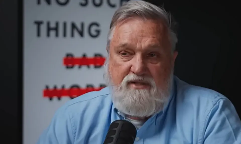 Doug Wilson, a middle-aged white man with gray hair and beard, is seated and speaking into a microphone. Partially visible behind him is an image of the cover of his book, "No Such Thing as Bad Words"