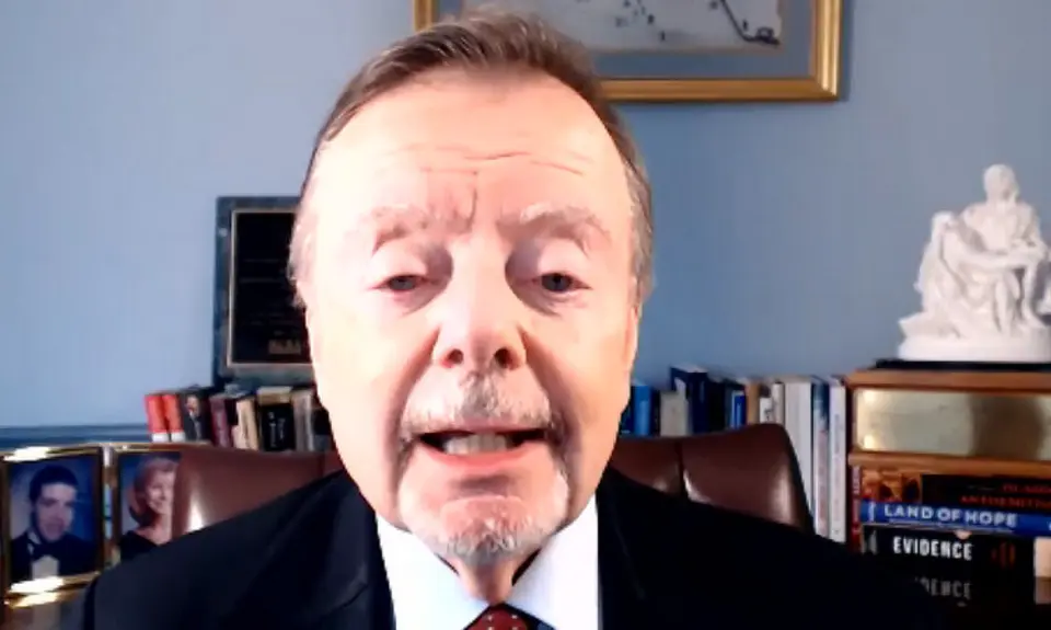 Gary Bauer, in suit and tie, is seated in what appears to be a home office. Visible behind him are some books and photos and a small model of what appears to be Michelangenlo's Pietà