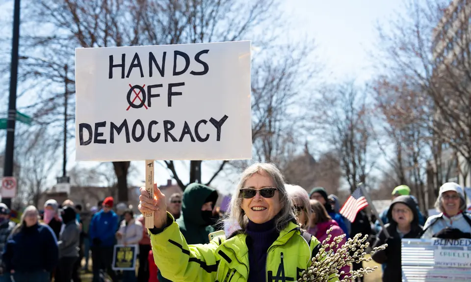 protestors holding a sign that says "hands off democracy"