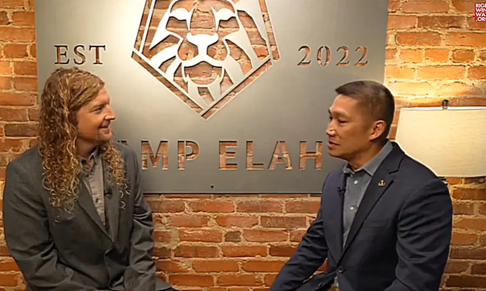 MAGA musician Sean Feucht and then-Senate candidate Hung Cao are seated in front of a brick wall on which is huge a large sign identifying their location as "Camp Elah," the Capitol Hill outpost for Feucht's political activities.
