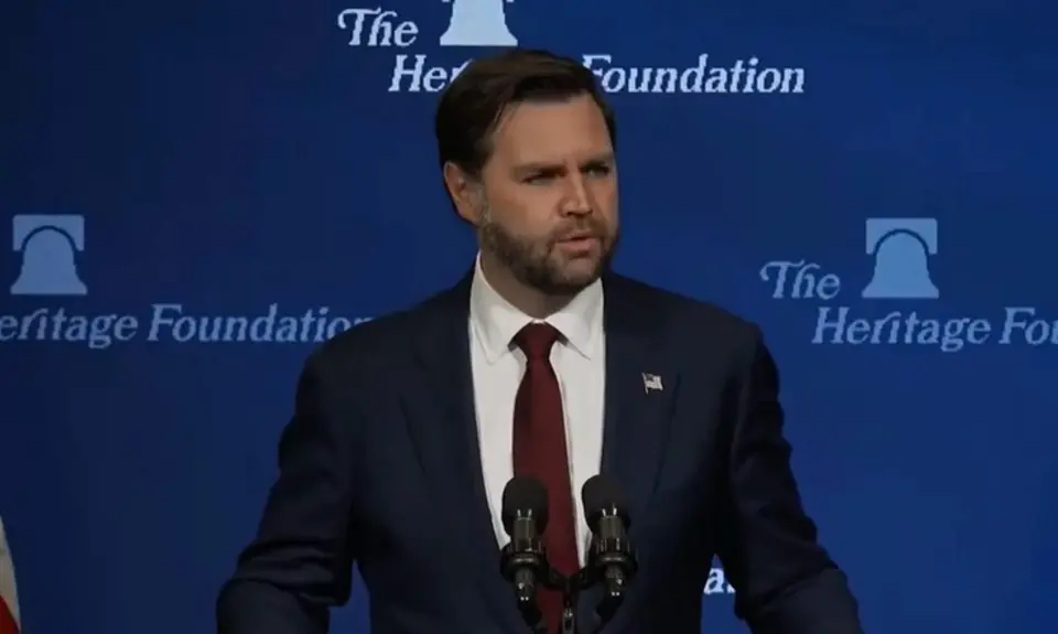 J.D. Vance, wearing suit and tie, stands behind lectern with Heritage Foundation logo behind him.