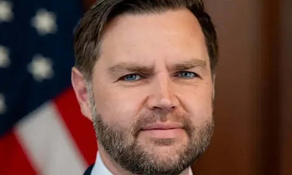 Close-up photo portrait of J.D. Vance with a blurry US flag visible behind him 