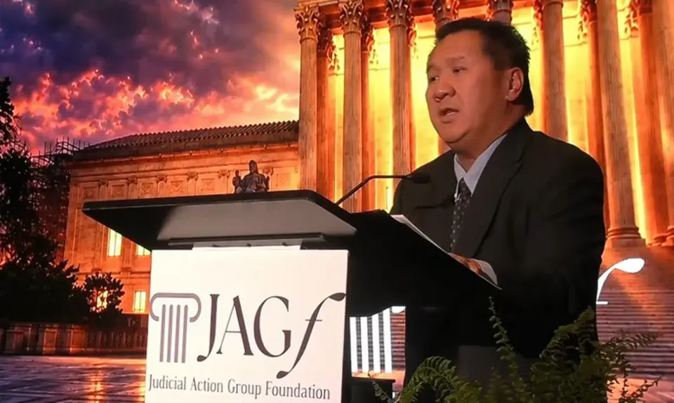 Judge James Ho stands behind lectern bearign logo of Judicial Action Network Foundation in front of backdrop image of U.S. Supreme Court lit dramatically at nightn