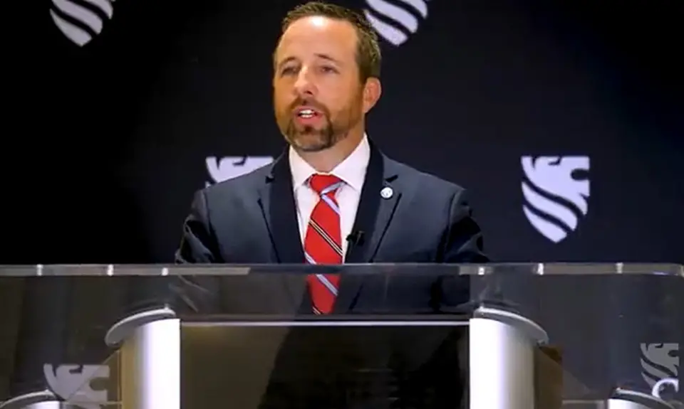 Josh Buice (pronounced Bice) in suit and tie stands at lectern in front of background bearing logo of the right-wing group Sovereign Nations
