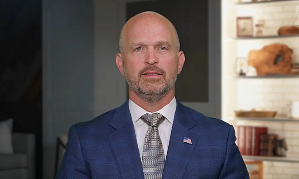 Heritage Foundation President Kevin Roberts, in suit and tie, speaks into a camera standing in what looks like an office, with a bookshelf behind him.
