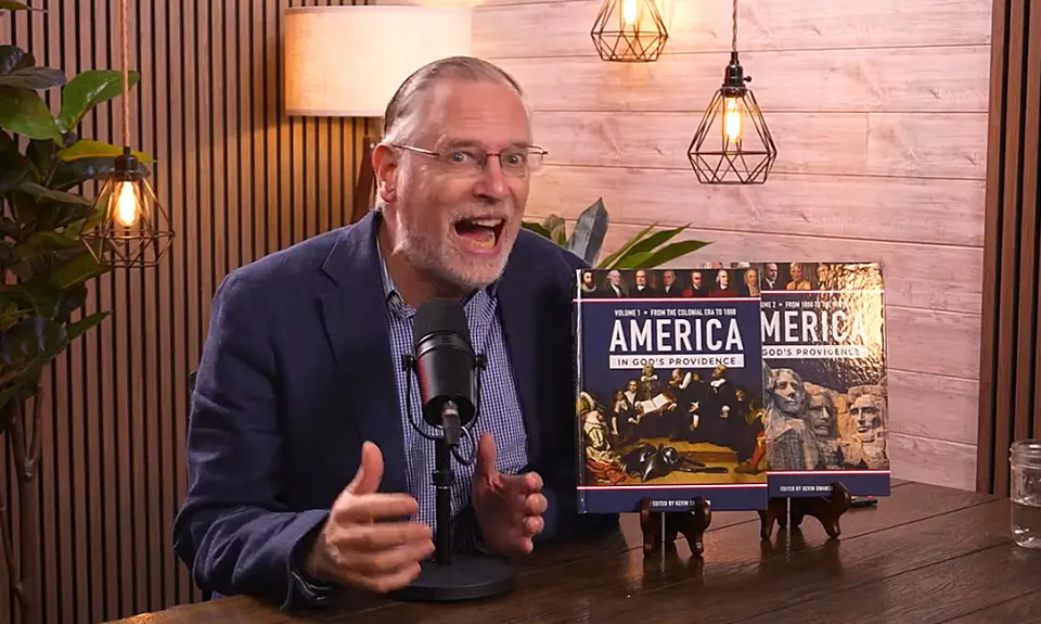 Kevin Swanson speaks animatedly into a microphone; two copies of his 1,000 page textbook on America's "Christian history" are propped up on the table next to him. 