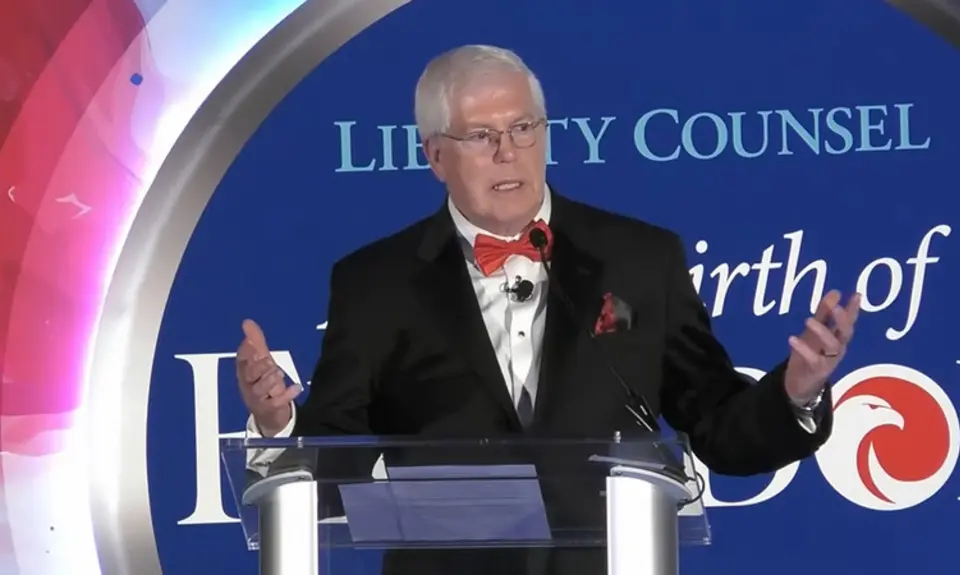 Mat Staver, a white man wearing a suit and red bowtie, gestures while speaking at lectern in front of logo for Liberty Counsel's 2025 gala and its theme "A New Birth of Freedom"