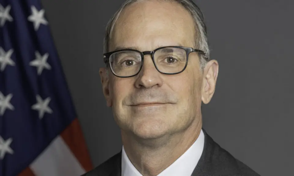 Formal portrait photo of Michael Anton in suit and tie looking into the camera with an American flag behind his right shoulder