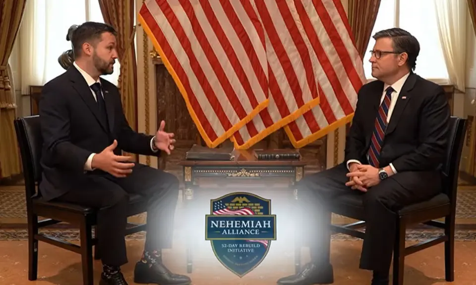House Speaker Mike Johnson and Pastor Tyler Feller are seated and facing each other in front of several American flags; the shield-shaped logo of the Nehemiah Alliance is superimposed on the screen in the foreground
