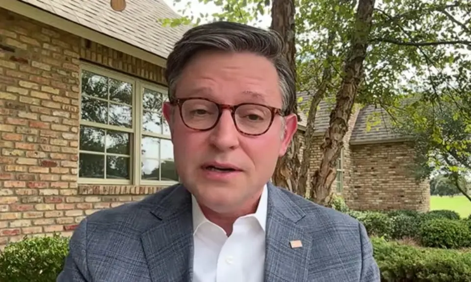 Mike Johnson, wearing suit jacket but no tie, is seated in his Louisiana back yard, with trees and his brick house visible behind him.