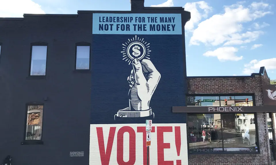 A mural with a handle holding a coin and text that reads "Leadership for the many, not for the money" and "Vote!"