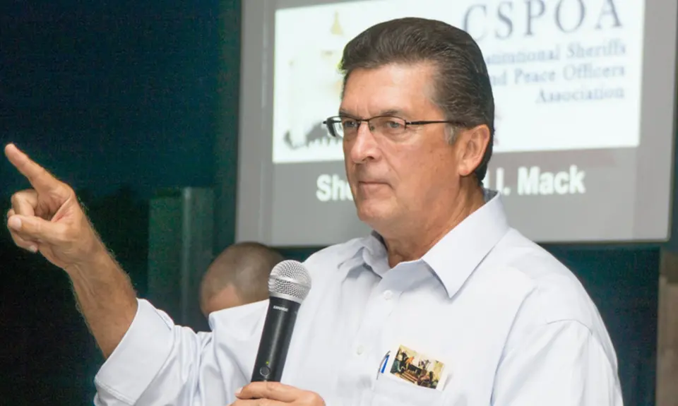 Photo of Richard Mack holding a microphone and pointing while speaking to an audience 