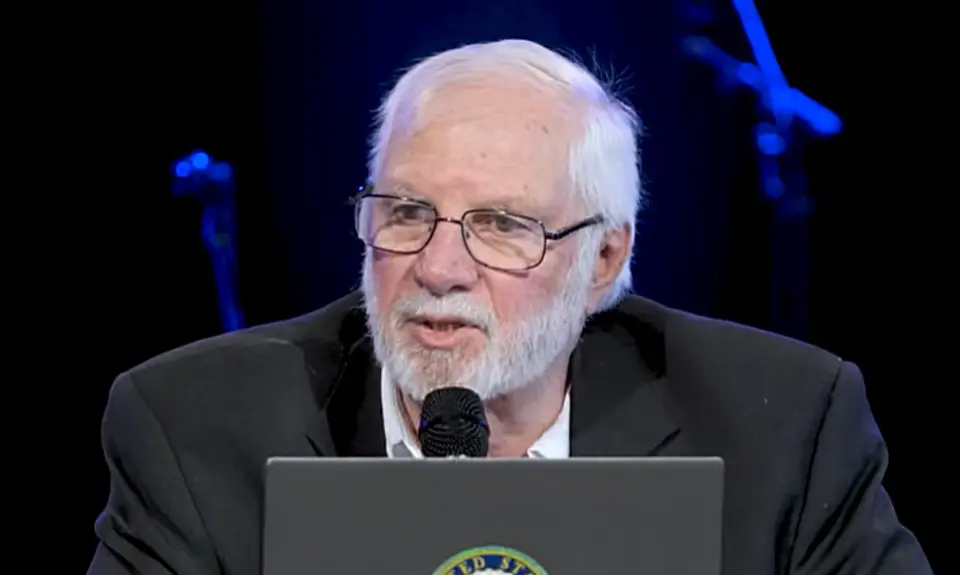 Rick Joyner preaching into a microphone while seated onstage with his laptop in front of him. s laptop.