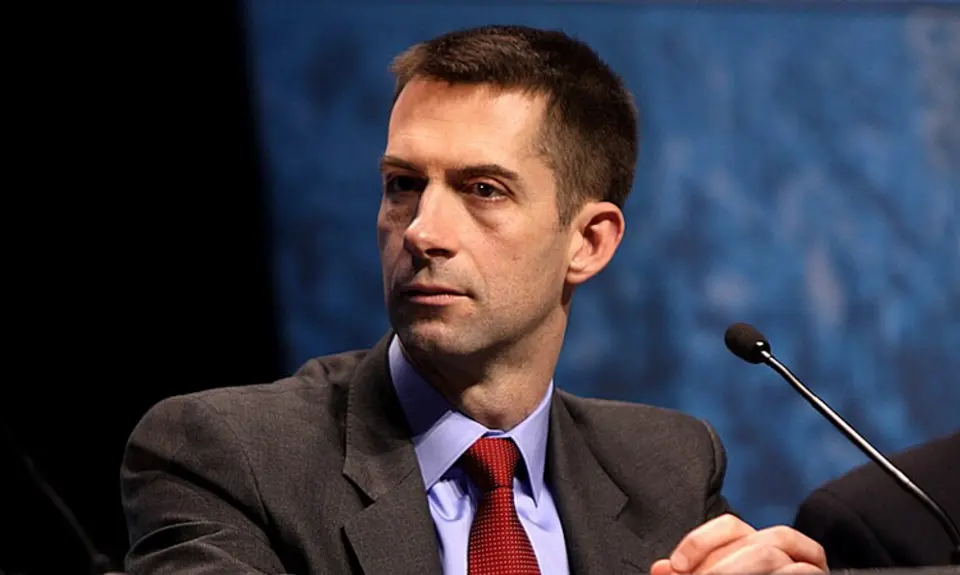 Photo of Sen Tom Cotton in suit and red tie seated at a microphone.