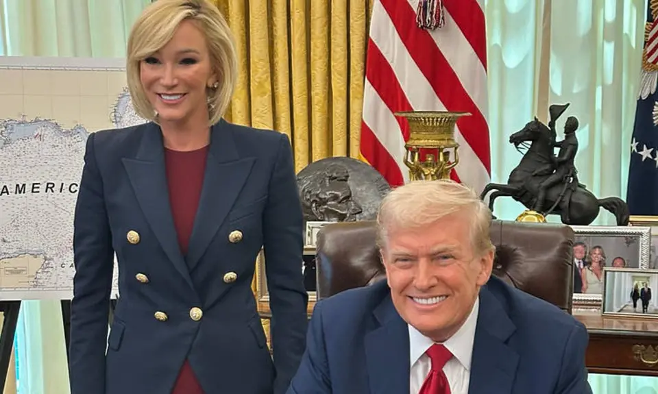 Donald Trump is seated at his desk in the Oval Office, with White standing next to and slightly behind him, both smiling for the camera. Partially visible behind White is a map on an easel touting the "Gulf of America."
