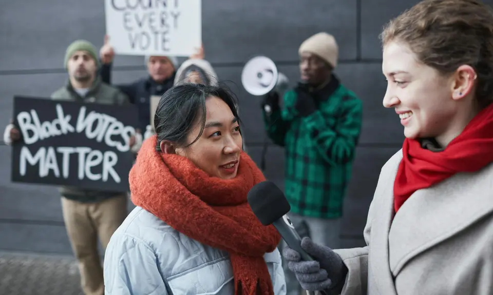 A reporter with a microphone interviews voting rights protestors