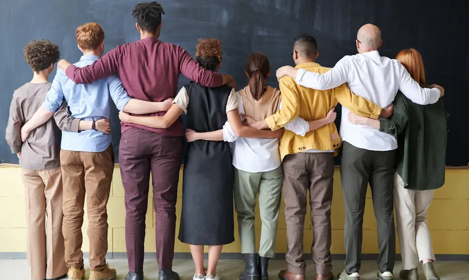 A group of people stand in front of a blackboard with their arms around each other