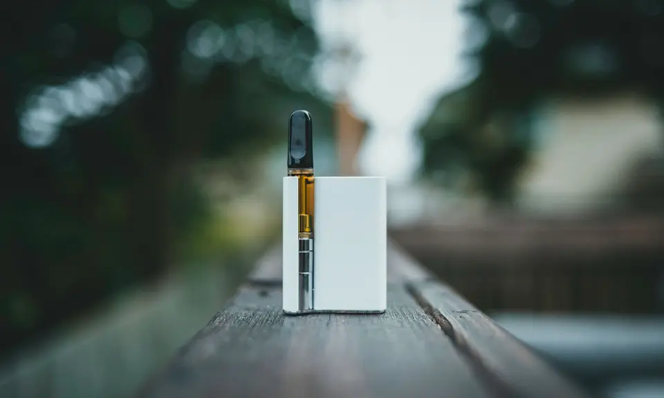 A photo of a white vape cartridge sitting on a fence