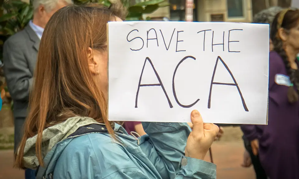 A woman holds a sign that says "Save the ACA"