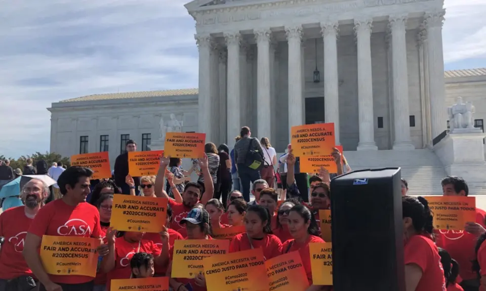 Activists stand outside the Supreme Court wearing red and carrying signs that read "America needs a fair and accurate #2020Census."