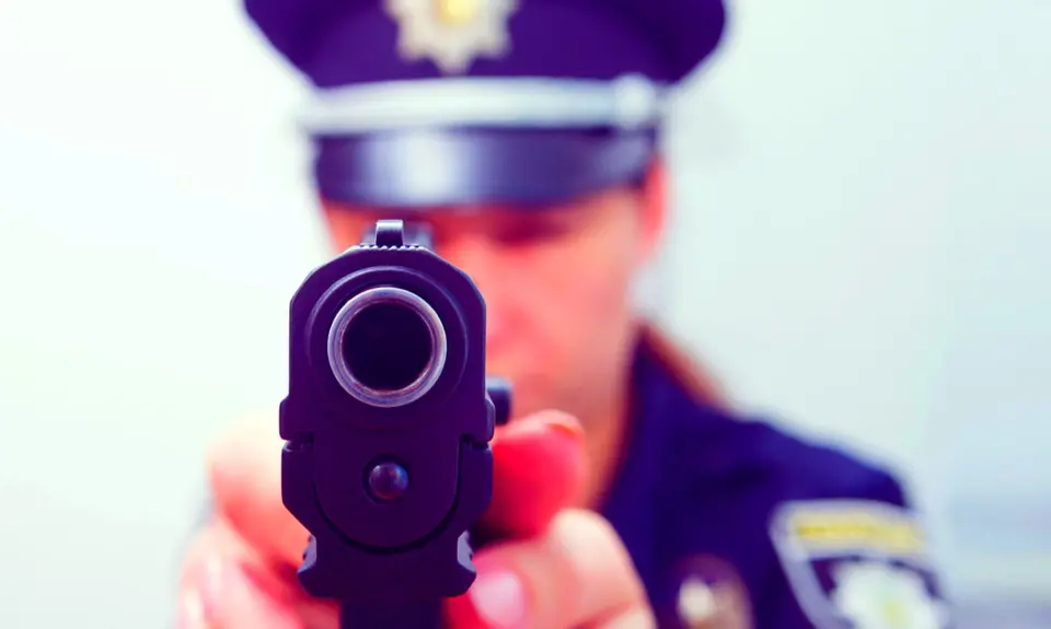 A police officer aims a gun directly at the camera