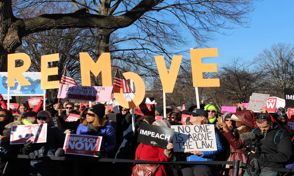 A group of rally-goers hold signs stating "Impeach now," "Impeach," and "No one is above the law" outside the Capitol Building in December 2019.