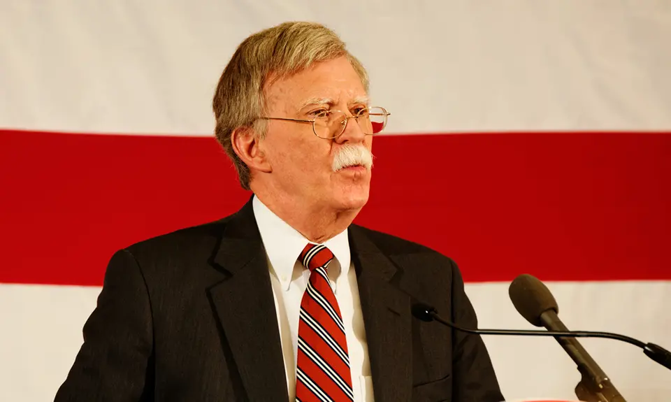 John Bolton stands at a podium in front of an American flag