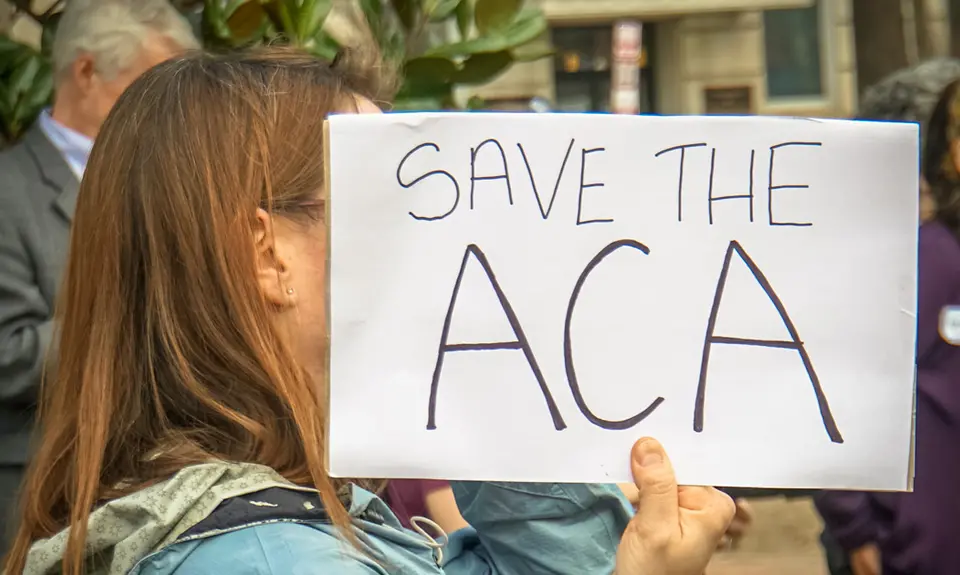 A woman holds a sign that says "Save the ACA"