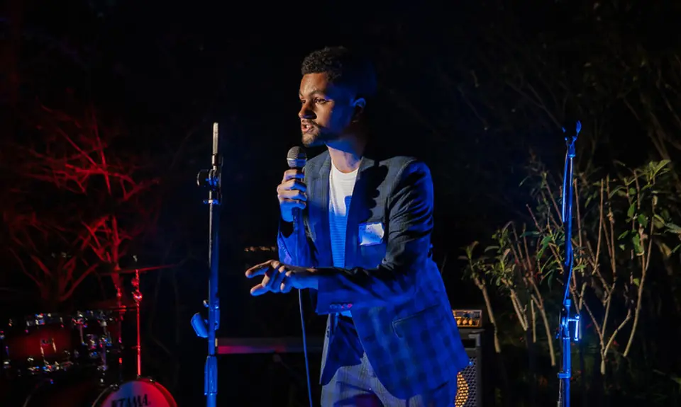Rep. Maxwell Frost holds a microphone and speaks on a stage with musical equipment.