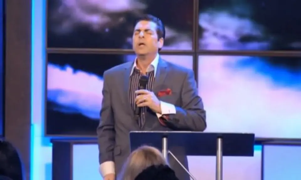 Hank Kunneman holding a microphone and standing at a podium.