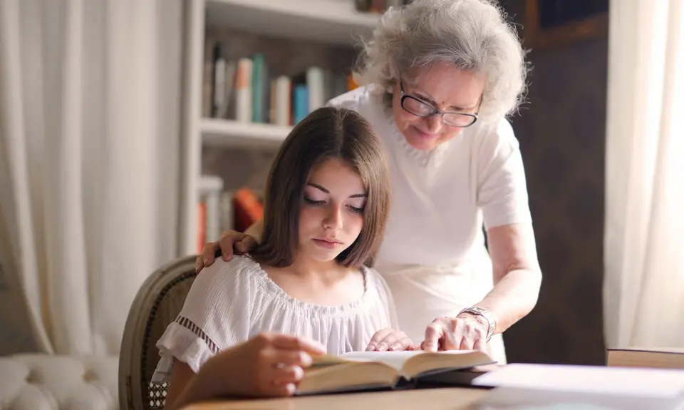 A grandmother helping her granddaughter read a book.