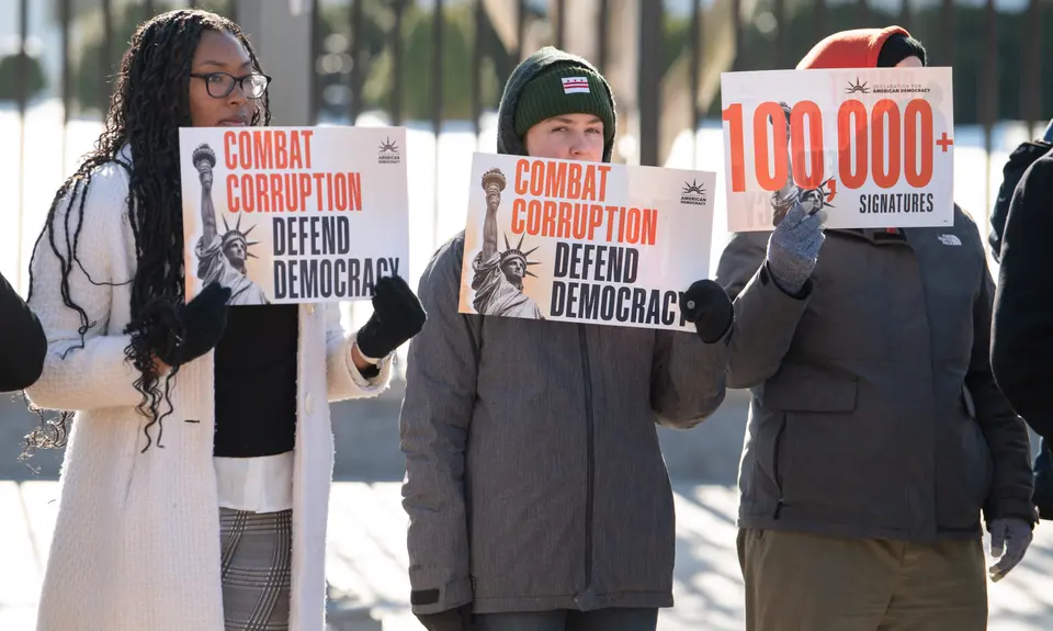 Three people hold signs reading "combat corruption, defend democracy"