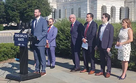 Photo shows Rep. Clay Fuller (R-GA) standing outside the US Capitol at a lectern with a sign that says "End SPLC Hate." Lined up behind him are five other people who spoke at the press conference, four men and one woman. 