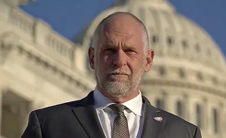 IFA President David Kubal, a balding white man in suit and tie, looks sternly into the camera with the US Capitol dome visible behind him. 