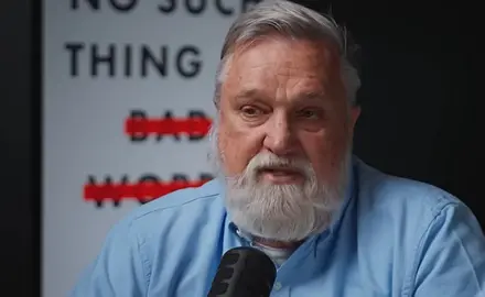 Doug Wilson, a middle-aged white man with gray hair and beard, is seated and speaking into a microphone. Partially visible behind him is an image of the cover of his book, "No Such Thing as Bad Words"