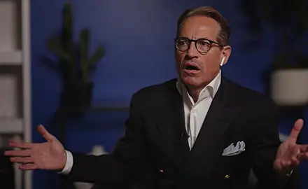 Metaxas gestures with both arms open while sitting in what appears to be a living room or home office