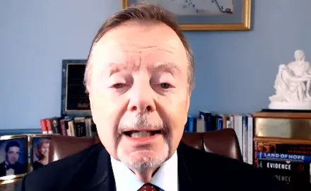 Gary Bauer, in suit and tie, is seated in what appears to be a home office. Visible behind him are some books and photos and a small model of what appears to be Michelangenlo's Pietà