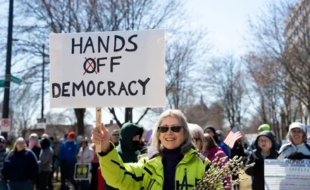 protestors holding a sign that says "hands off democracy"