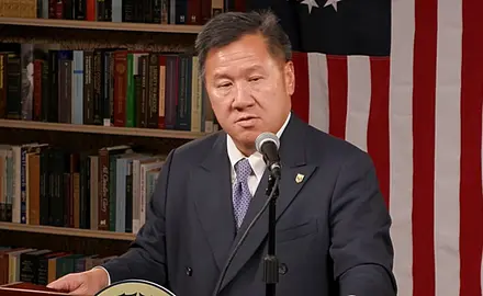 James Ho, in a suit and tie, speaks at a lectern with a U.S. flag visible behind him