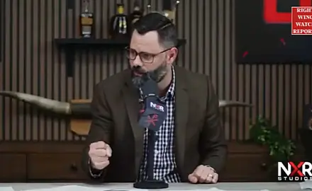 Joel Webbon, seated in his studio, clenches his right fist