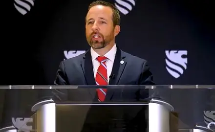 Josh Buice (pronounced Bice) in suit and tie stands at lectern in front of background bearing logo of the right-wing group Sovereign Nations
