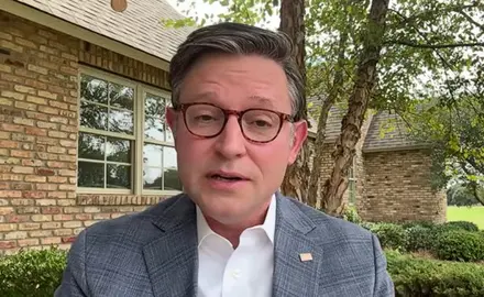 Mike Johnson, wearing suit jacket but no tie, is seated in his Louisiana back yard, with trees and his brick house visible behind him.