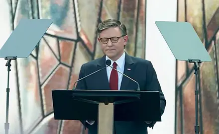 House Speaker Mike Johnson pictured standing at a lectern on the outdoor stage at the Rededicate 250 event.
