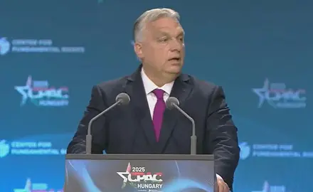 Viktor Orban stands at a lectern with logo for CPAC Hungary 2025, the logo is also visible on the backdrop behind him. 