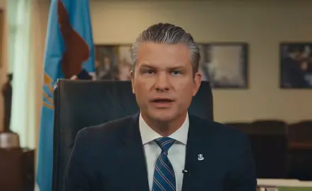 Pete Hegseth, wearing suit and tie, is seated in his office and speaking into the camera.