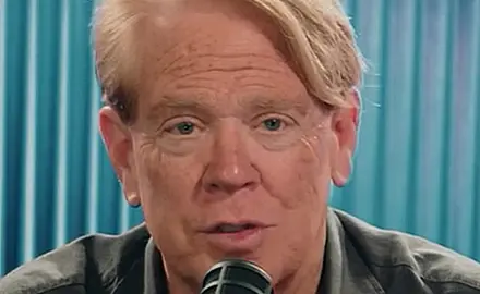 Close-up image of white man with reddish blonde hair speaking into a microphone.