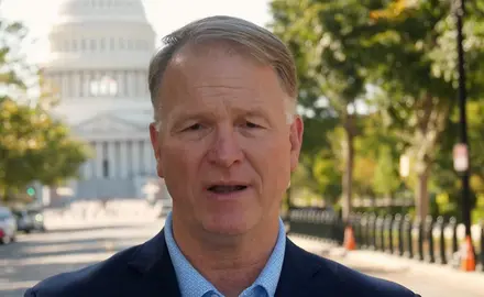 Phillip Jauregui is speaking into the camera while standing outdoors with the U.S. Capitol visible behind him. 