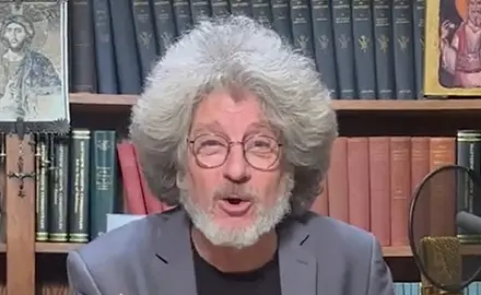 Randall Terry, white man with gray beard and full head of feathered gray hair, is seated at a microphone in front of bookshelves.